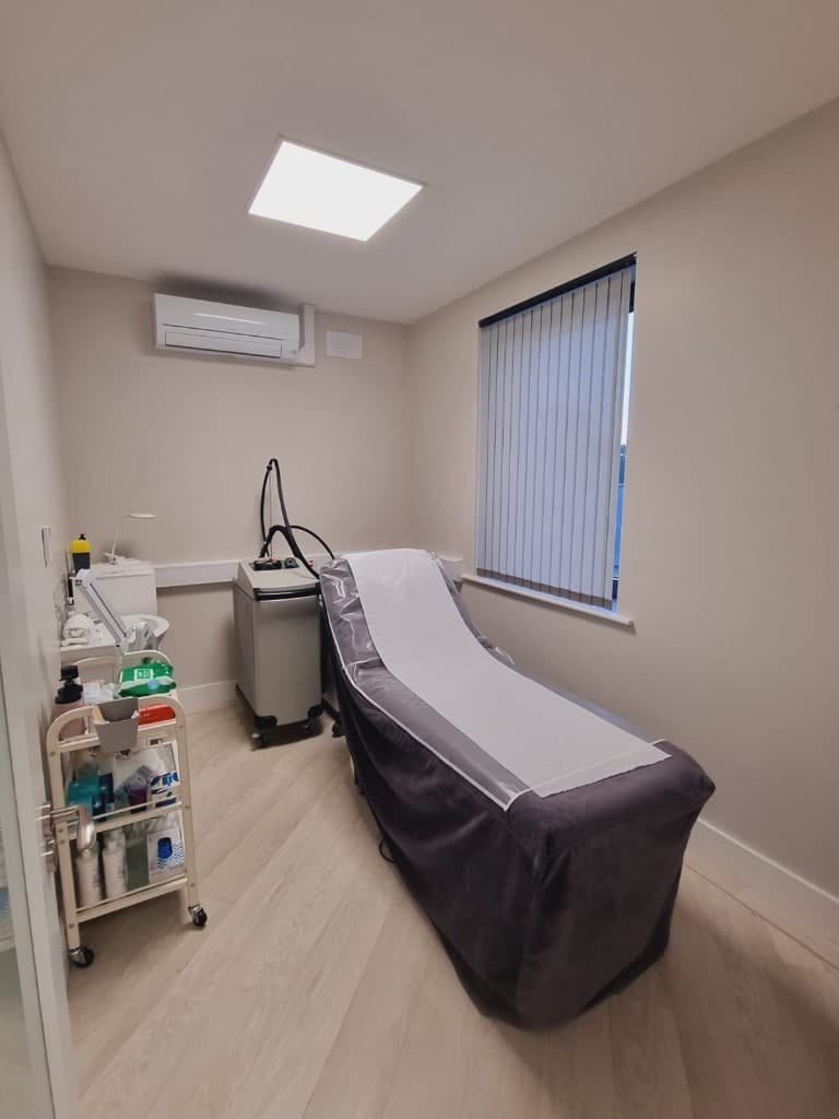 A clinical treatment room at Skin Laine in Ballina with a prepared bed, aesthetic device, and supply cart.